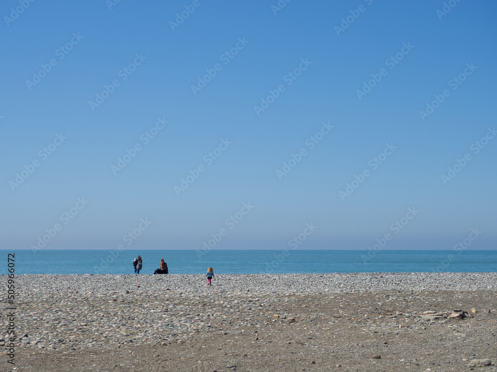 People are far away on the pebble beach. Rest on the sea. Loneliness.