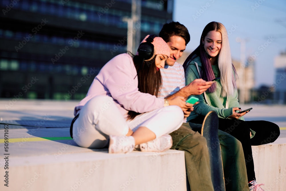 Obraz premium Three teenage friends are sitting in the urban exterior and hanging on their phones.