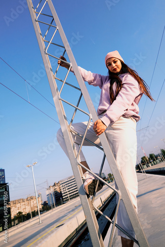 Rebellious teenage girl climbing on the metal construction at the train station.