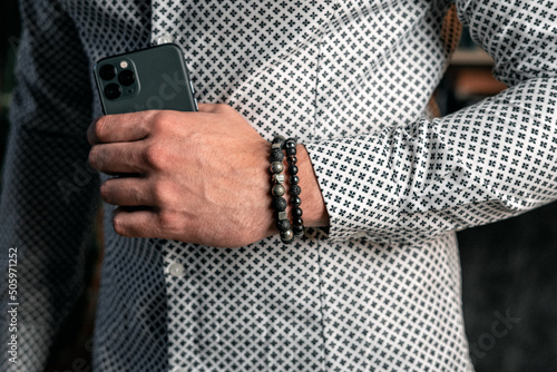 Strong male hand holding a phone. Bracelets made of natural stones © ChocolateShot