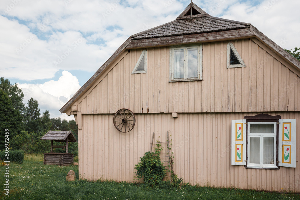 Naklejka premium Old traditional wooden house with windows and shutters, rear view. An old carriage wheel is hung on the wall, the roof is covered with wooden tiles.