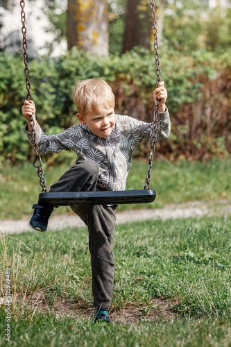 Fotografie A little self-sufficient boy tries his best to climb a chain swing in a city park