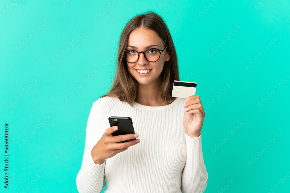 Young woman over isolated blue background buying with the mobile with a credit card Young woman over isolated blue background buying with the mobile with a credit card
