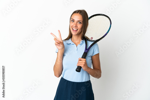 Woman playing tennis over isolated white wall smiling and showing victory sign