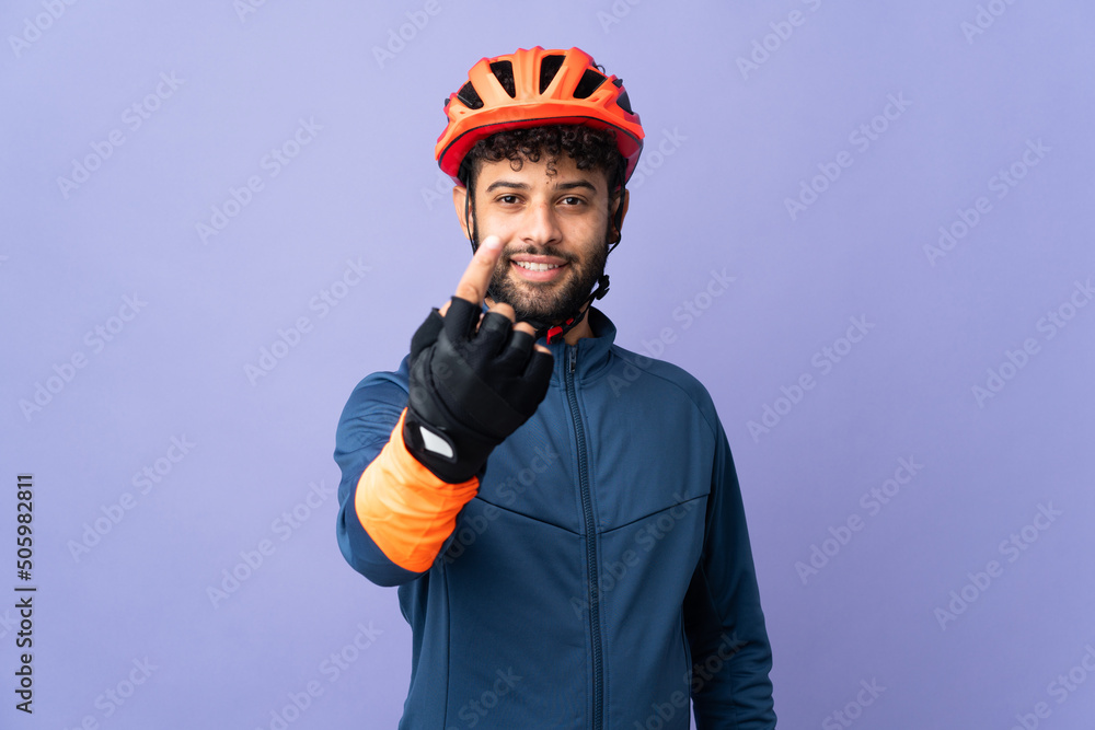 Young Moroccan cyclist man isolated on purple background doing coming gesture Young Moroccan cyclist man isolated on purple background doing coming gesture