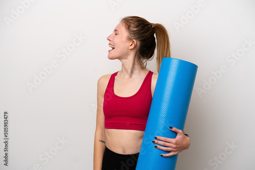 Young sport English woman going to yoga classes while holding a mat isolated on white background laughing in lateral position