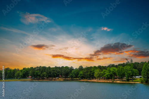 a gorgeous blue rippling lake surrounded by lush green trees, grass and plants with powerful red clouds at sunset at Lake Spivey Recreation Center in Jonesboro Georgia USA photo