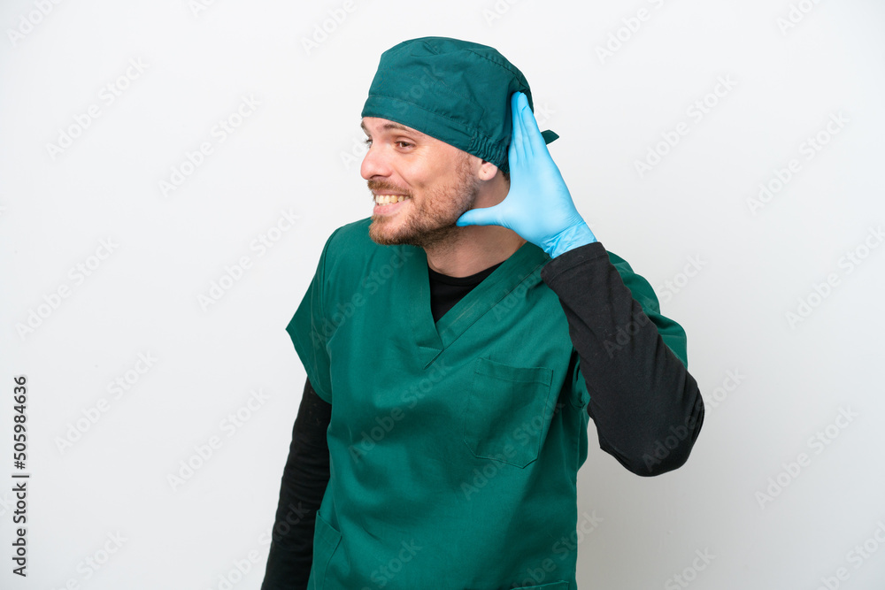 Surgeon Brazilian man in green uniform isolated on white background listening to something by putting hand on the ear