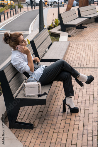 non-binary man talking using phone in her hands leaning on park bench in the street