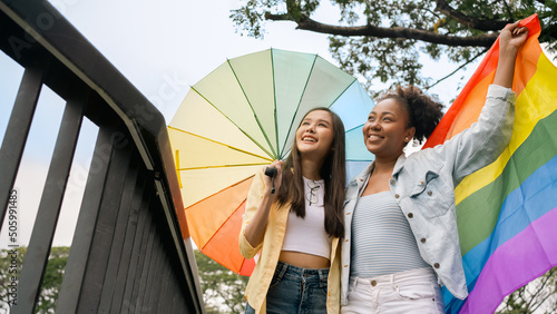 Women Group enjoying holding Rainbow LGBT Pride flag.Smiling multi ethnic female enjoying displaying anti-racism symbols for LGBT rights. Diversity,tolerance and gender identity concept.African,Asian. photo