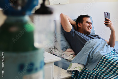 A happy sick Mexican man with a ventilator and an oxygen tank makes a video call on his phone
