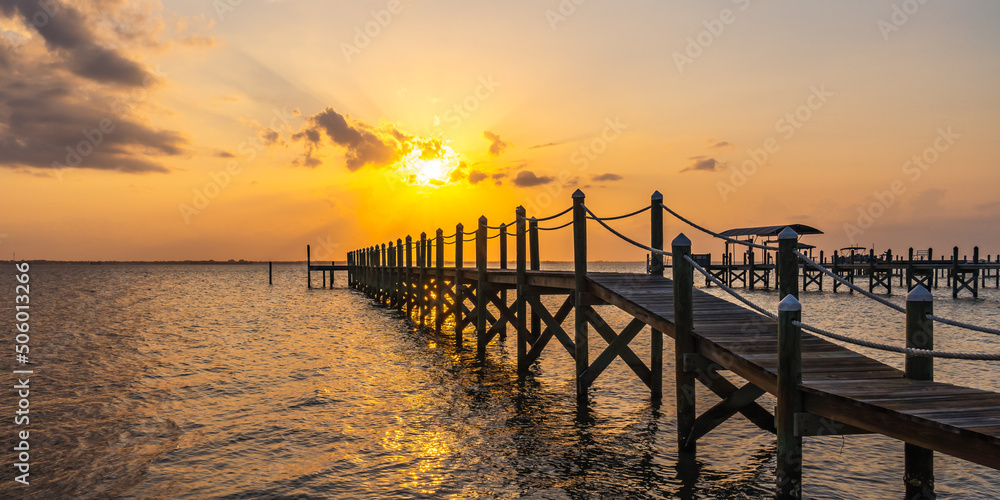 Fototapeta premium Wooden pier on poles with rope railings during a yellow sunset over the Indian River, Vero Beach, Florida