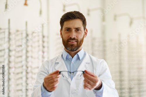Portrait of handsome ophthalmologist offering glasses to client in optics store