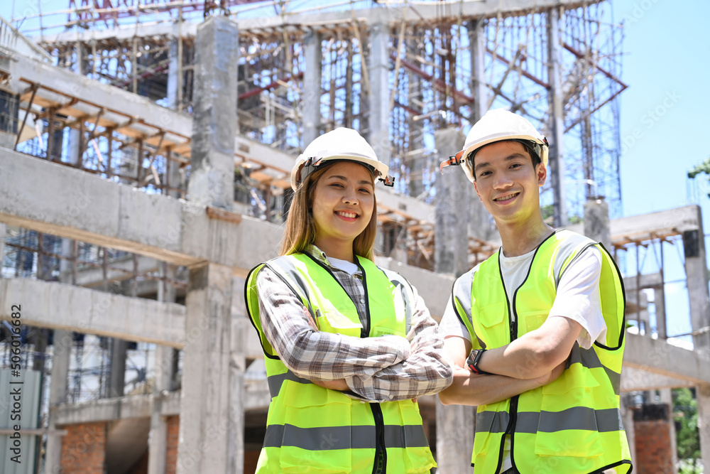 Architect and construction engineer wearing safety helmet standing with arms crossed at construction site. Industry, Engineer, construction concept Architect and construction engineer wearing safety helmet standing with arms crossed at construction site. Industry, Engineer, construction concept