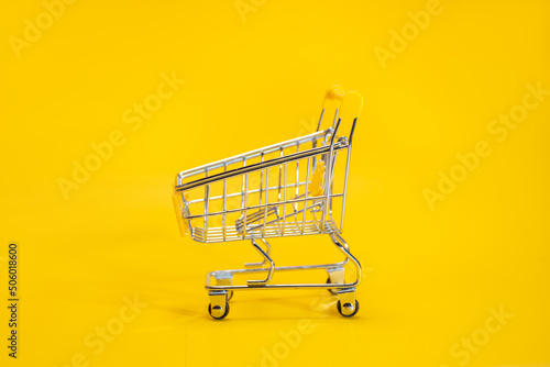Metal empty trolley or shopping cart for groceries on a yellow background: place for text for big sale and sale online concept