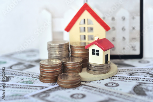 small red roof house on the stacking coins around with the dollar bills and transparent calculator background for calculate the home payment interest of  house loan monthly installment. photo