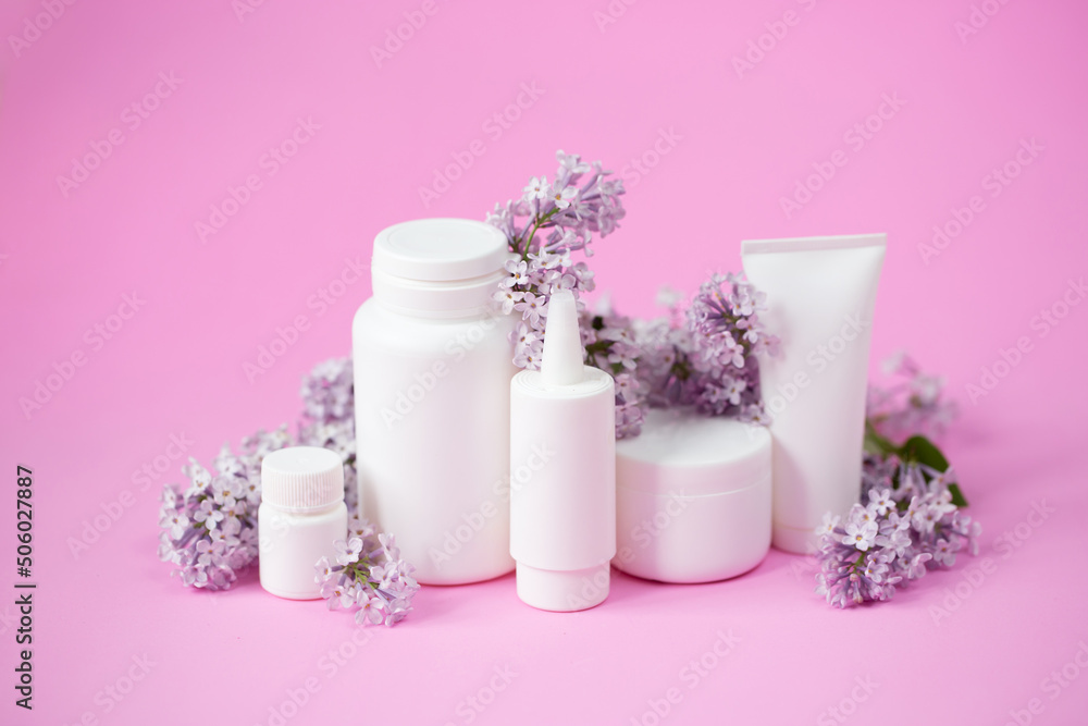 Face and body skin care. A set of cosmetic creams and balms in white tubes and cans on a coral background with sprigs of lilac flowers. Spa treatments for home care. Home rejuvenation and moisturizing Face and body skin care. A set of cosmetic creams and balms in white tubes and cans on a coral background with sprigs of lilac flowers. Spa treatments for home care. Home rejuvenation and moisturizing