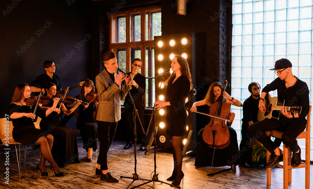 Fototapeta premium Music rock band with string quartet on the background of the loft interior sing and play instruments