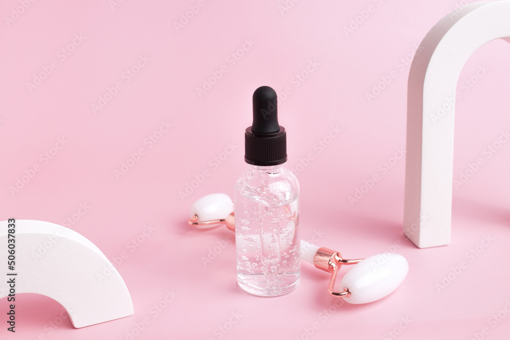 Glass bottle with oil, roller for face massage on a pink background with arch. Cosmetic facial skin care and spa. Natural treatment concept.