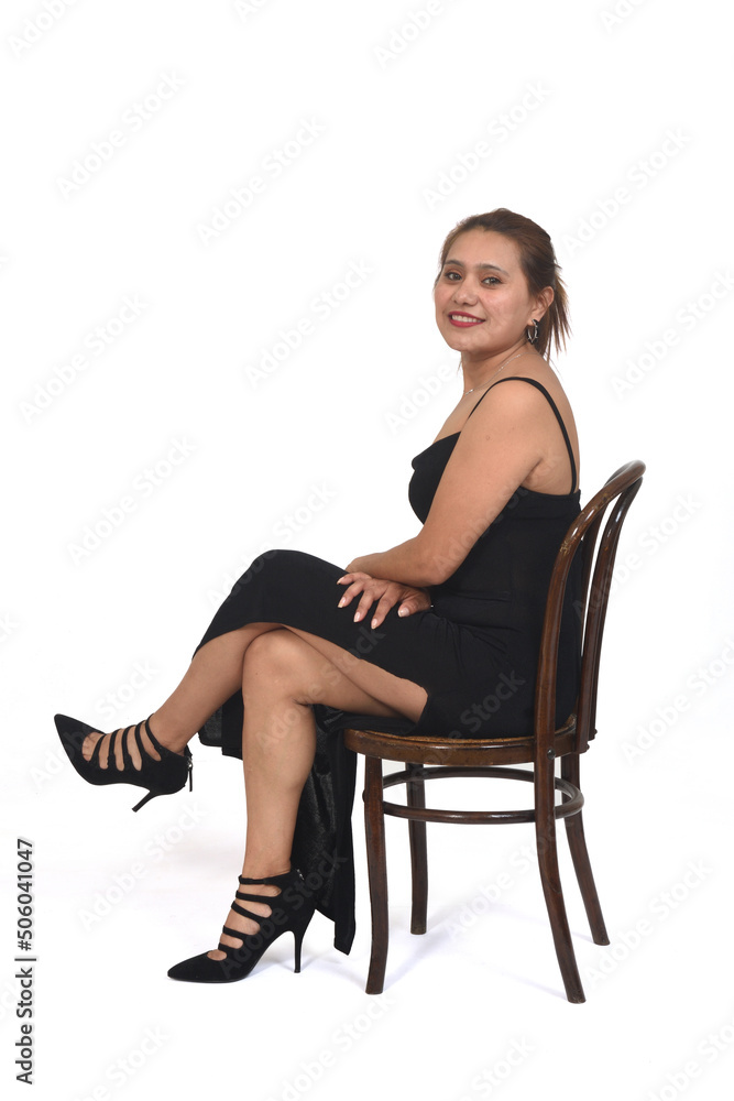 side view of a woman sitting on chair with dress and heeled shoes looking at camera and legs crossed on white background side view of a woman sitting on chair with dress and heeled shoes looking at camera and legs crossed on white background