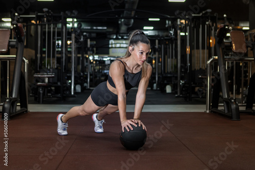 Serious fit sportswoman doing medicine ball plank exercise in gym