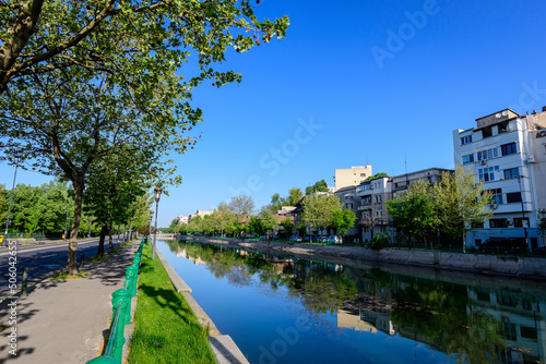 Landscape with large green old trees near Dambovita river and clear blue sky in the center of Bucharest, Romania, in a sunny spring day.