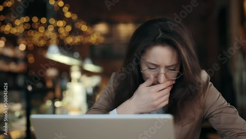 Caucasian woman with brown hair coughing in fist while sitting at cafe with modern laptop. Health condition, people and work concept. photo