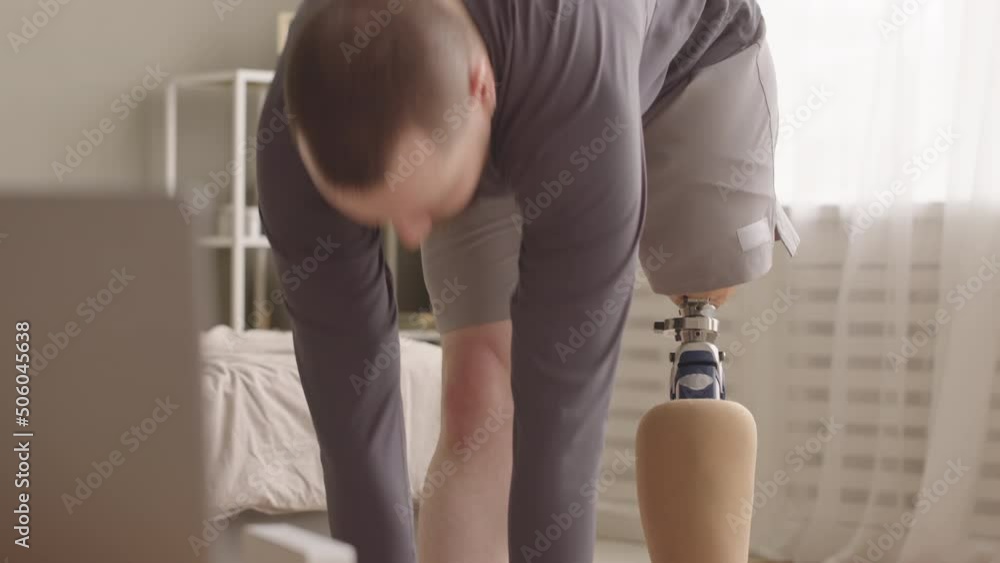 Slowmo of Caucasian man with prosthetic leg bending forward while training at home via laptop Slowmo of Caucasian man with prosthetic leg bending forward while training at home via laptop