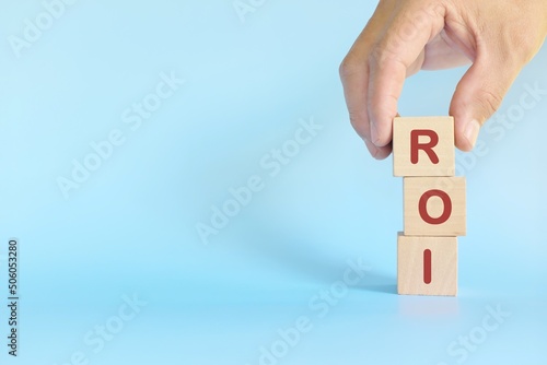 Hand stacking wooden blocks with ROI letters. Return on investment business growth concept.