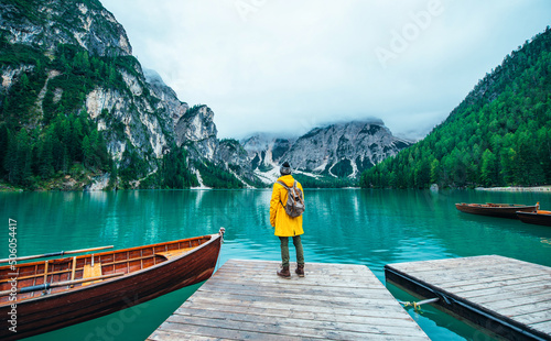 Mountain stories. Happy backpacker on a wanderlust vacation. Man with a yellow raincoat standing in front the lake and enjoying the view