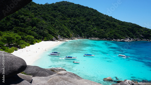 Turquoise water in the bay. View of the island and the sea. High cliffs covered with green trees. The gradient of water from blue to blue. There are speedboats, people swim in places. Similan Islands