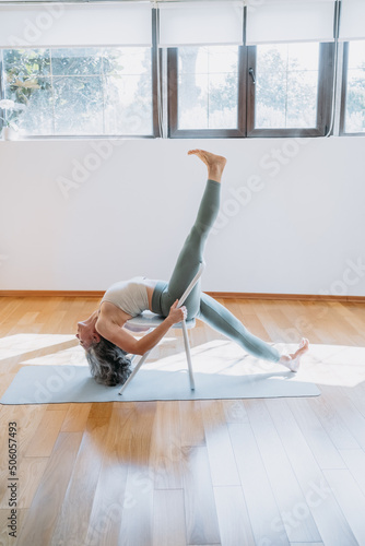 Mature skinny sportive flexible woman sitting on chair in her home during quarantine. stretching in yoga studio. What to do at home during self-isolation. Stay home concept