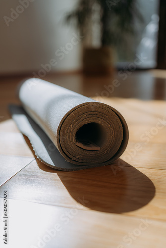 Rolled up yoga or pilates mat for exercise on natural wooden floor, sport class before or after practicing yoga, preparing for exercise, closeup