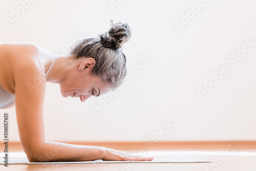 Side view of the senior healthy woman workout at home, making exercise, doing yoga, standing at the plank. Home fitness concept