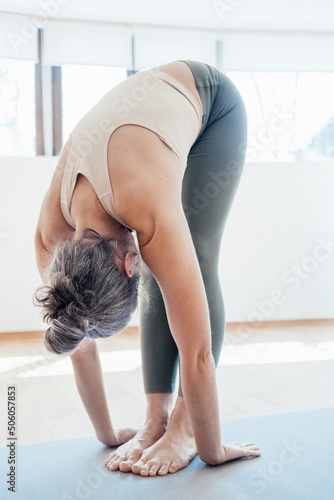 Full length view of the elderly woman practicing yoga, standing in head to knees pose, working out at home. Stock photo