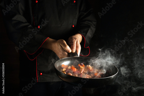 Fototapeta Naklejka Na Ścianę i Meble -  The chef prepares food in a frying pan with steam. The concept of restaurant and hotel service