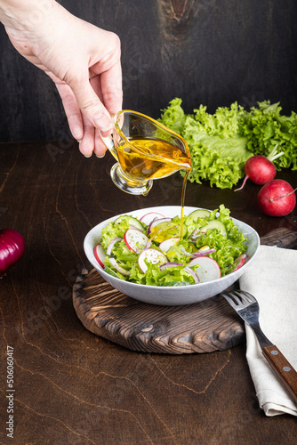 Woman hand dressing fresh vegetable salad with olive oil on wooden background