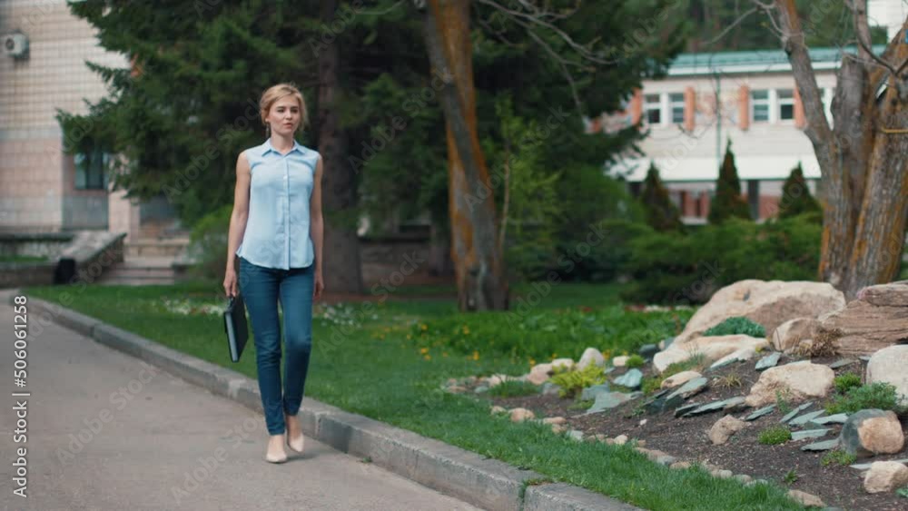 A business woman in a light blouse and carrying a briefcase for documents goes to her office. Blonde lady walks through the summer city. Slow motion. A business woman in a light blouse and carrying a briefcase for documents goes to her office. Blonde lady walks through the summer city. Slow motion.
