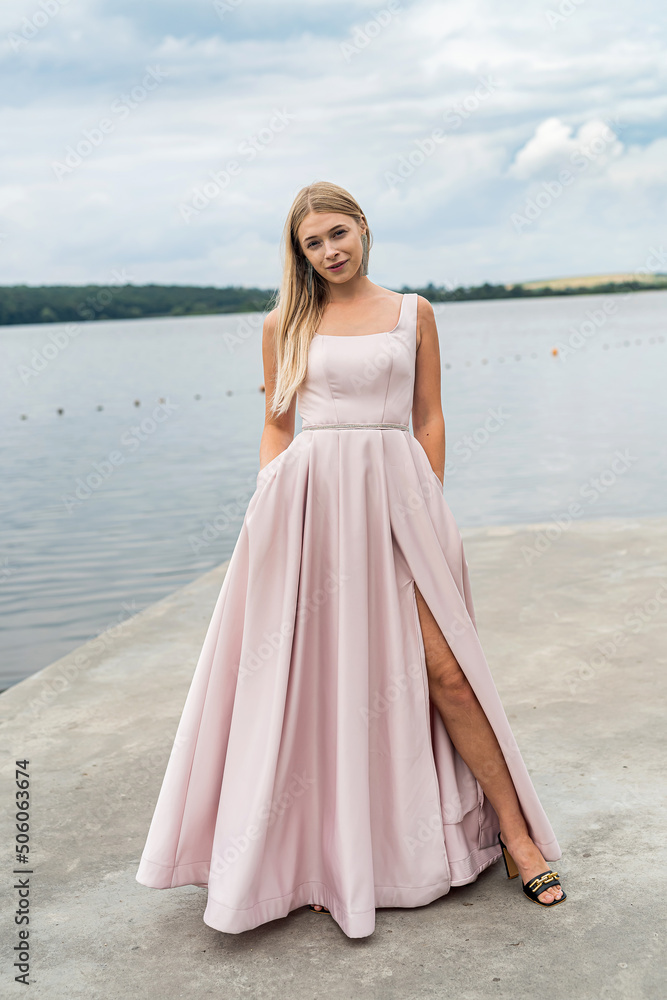 Young woman enjoying summer time posing alone in cute ping dress near lake Young woman enjoying summer time posing alone in cute ping dress near lake