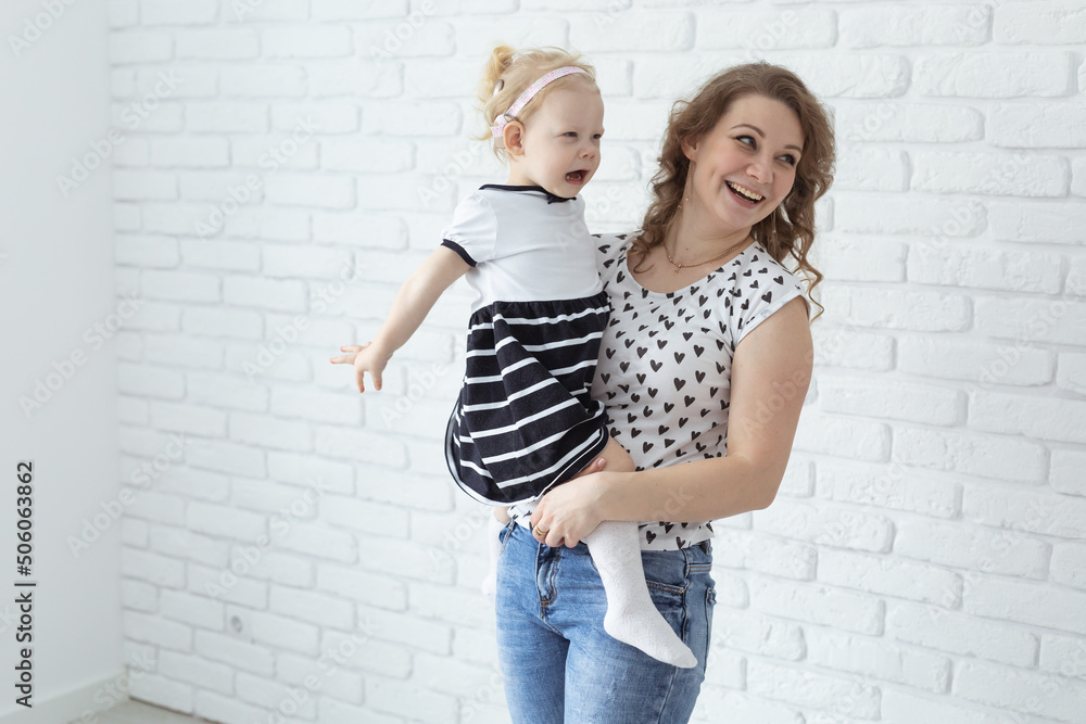 Mother holds and having fun child with hearing aids and cochlear implants on white brick wall with copy space . Deaf and diversity and innovating medicine technologies concept Mother holds and having fun child with hearing aids and cochlear implants on white brick wall with copy space . Deaf and diversity and innovating medicine technologies concept