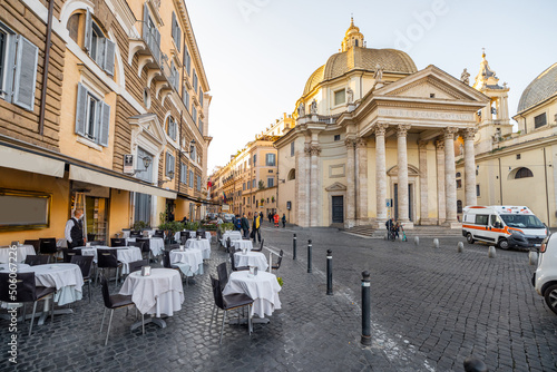 Cityscape of Piazza del Popolo, famous city square with restaurant tables and church in Rome. Morning view on sunny weather
