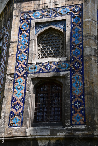 Windows with beautiful openwork lattices. Wall of an old building with colored tiles