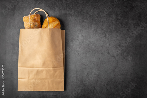 Disposable paper bag from a supermarket recyclable with whole baked loaves of bread flatlay on dark background with copy space.