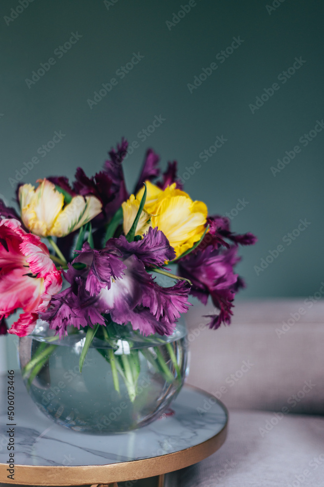 Beautiful Bunch of Parrot Style Tulips in Glass Fishbowl Vase at the coffee table in the living room on dark background, spring holiday concept, decorate your house with flowers Beautiful Bunch of Parrot Style Tulips in Glass Fishbowl Vase at the coffee table in the living room on dark background, spring holiday concept, decorate your house with flowers