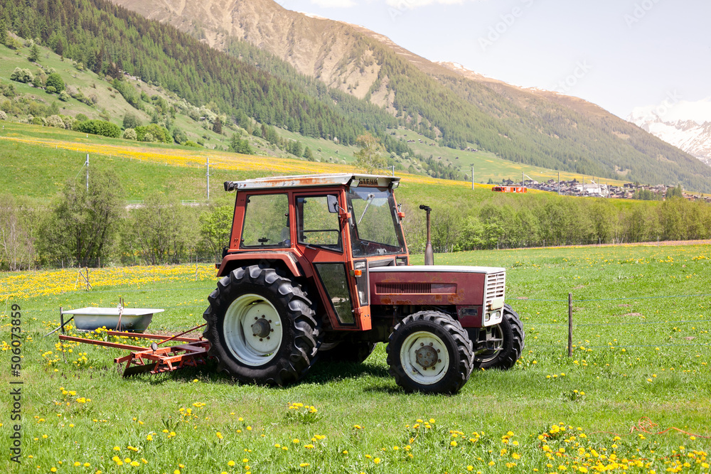 Tractor in alpine village on a green meadow, mountains on the background Tractor in alpine village on a green meadow, mountains on the background