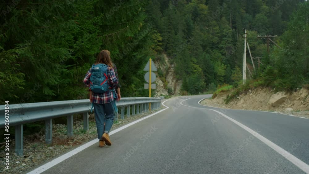 Couple hitchhikers walk mountains. Two travelers trekking on roadside highway. Couple hitchhikers walk mountains. Two travelers trekking on roadside highway.