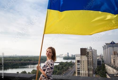 Ukrainian flag in the hands of a woman standing on the roof of a house in Kyiv above the buildings. National symbol of freedom and independence. Stop the war. A call for help to Ukrainians