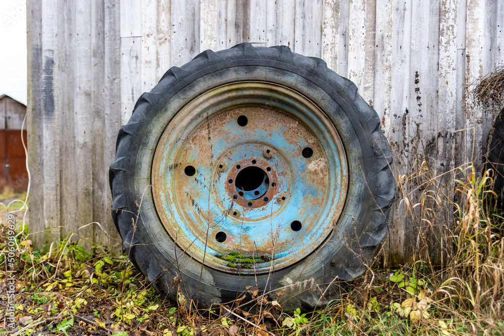 a large blue rusty wheel from a tractor stands near the wall of the barn a large blue rusty wheel from a tractor stands near the wall of the barn