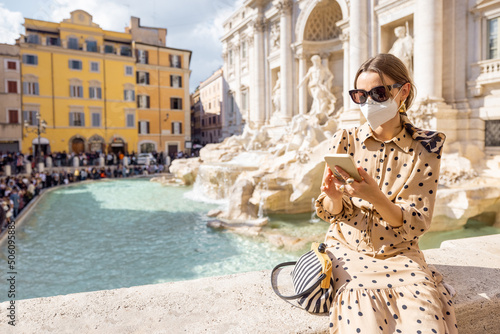 Woman in face mask visiting famous di Trevi fountain in Rome. Concept of new social rules when traveling. Social distancing and wearing mask in public places