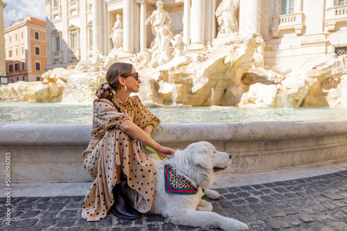 Woman sitting with dog on famous di Trevi fountain in Rome. Woman traveling with her white huge dog, visiting italian landmarks